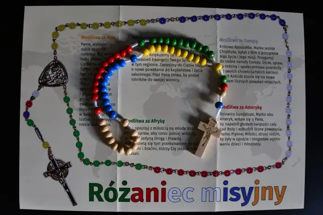 Kolorowy różaniec misyjny z drewnianym krzyżykiem i medalikiem, ułożony na kartce z modlitwami za różne kontynenty.