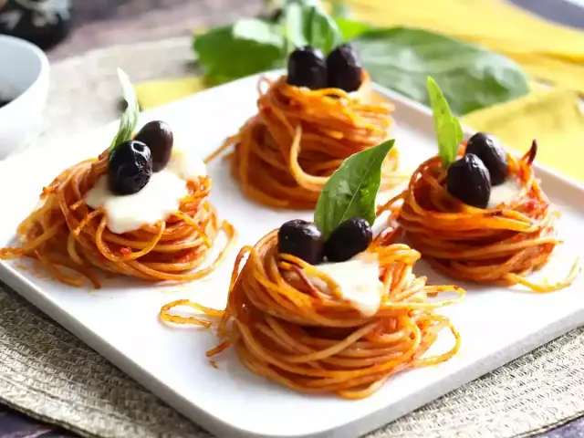 Cztery małe gniazdka spaghetti z oliwkami i bazylią. Idealne, by ustalić, ile gniazdek makaronu na osobę.