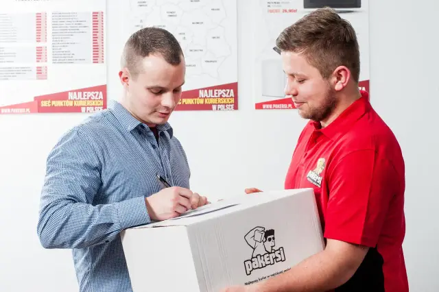 Kurier w czerwonej koszulce przekazuje paczkę, a klient podpisuje dokument. Zastanawiasz się, ile zarabia kurier?