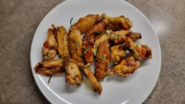 Alette di pollo in padella, dorate e succulente, guarnite con rosmarino fresco. Un piatto invitante pronto per essere gustato.
