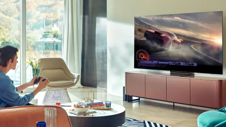 Młody mężczyzna gra w wyścigi na telewizorze 65 cali. Idealna odległość od telewizora 65 cali zapewnia immersję w grze.