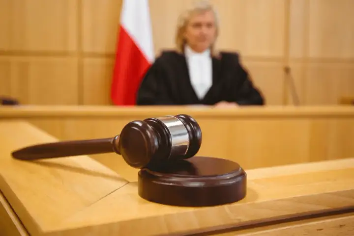 Młotek sędziowski na stole w sali sądowej, obok polska flaga. Sędzia w todze w tle. Ile apelacji jest oddalanych?