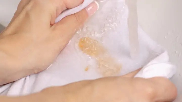 Hände waschen ein weißes Tuch mit Kaffeeflecken unter fließendem Wasser, um sie zu entfernen.