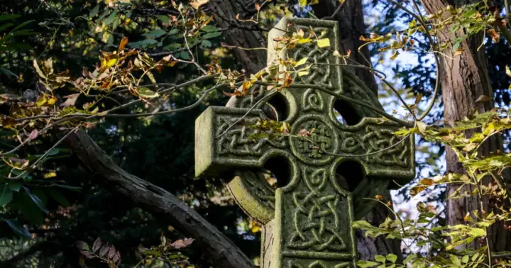 Kamienny krzyż celtycki z misternymi wzorami, otoczony jesiennymi liśćmi. Symbolizuje wieczność i połączenie życia.