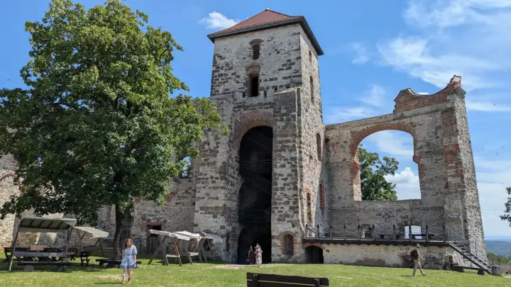 Ruiny zamku Tenczynek z wieżą i łukiem, na tle błękitnego nieba z chmurami.