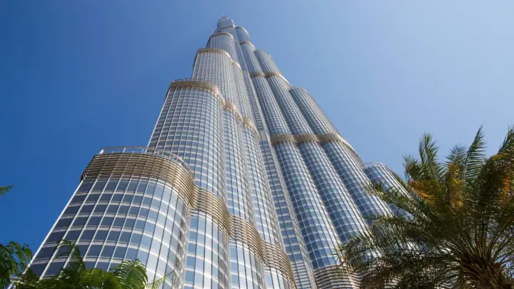 Burj Khalifa, najwyższy budynek na świecie, wznosi się ku błękitnemu niebu, otoczony palmami.