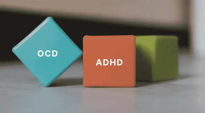 Tre färgglada kuber med texten ADHD och OCD. En blå kub med OCD, en orange med ADHD och en grön i bakgrunden.