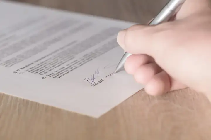 Podpisanie umowy kupna sprzedaży domu. Dłoń z długopisem składa podpis na dokumencie.