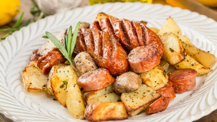 Pyszne dania z piekarnika na obiad: pieczone ziemniaki, kiełbaski i grzyby, doprawione ziołami i pieprzem.