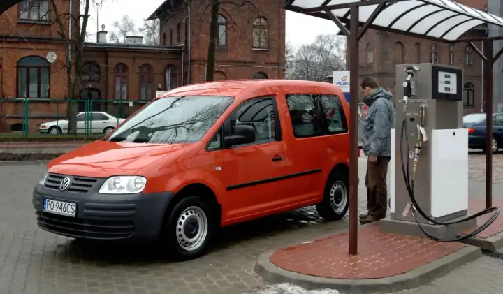 Pomarańczowy Volkswagen Caddy, auto zasilane CNG i hybrydą, tankuje na stacji.