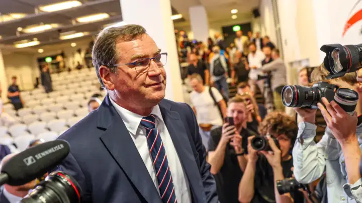 Mężczyzna w garniturze, jak kapitan reprezentacji Polski, otoczony przez fotoreporterów z aparatami.