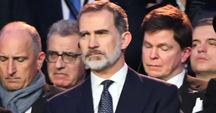 Król Hiszpanii Felipe VI w garniturze i krawacie, otoczony przez innych mężczyzn.