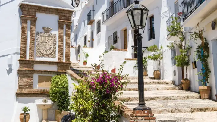 Escaleras empedradas y casas blancas adornadas con flores, un escudo de armas y una farola. Descubre qué ver en Frigiliana, un pueblo blanco andaluz.