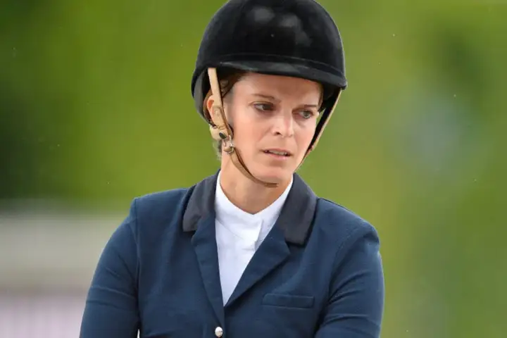 Athina Onassis w kasku i eleganckim stroju jeździeckim, skupiona na zawodach.