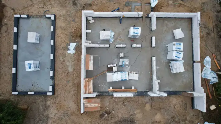 Budowa domu z bloczków betonowych. Materiały budowlane leżą na płycie fundamentowej, czekając na montaż ścian, by zapewnić niski współczynnik przenikania ciepła.