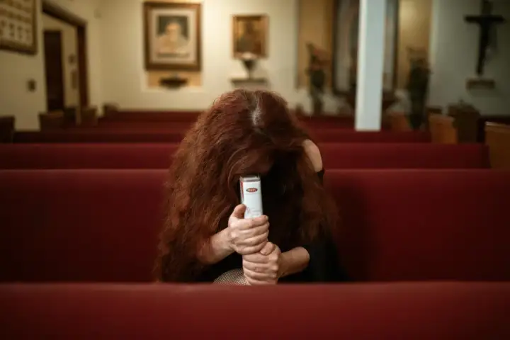 Kobieta z rudymi włosami, siedząca w kościele, trzyma Biblię. Objawy wypalenia u liderów grup religijnych jak zapobiegać.