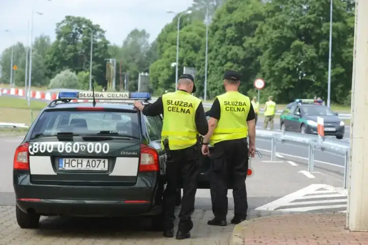 Funkcjonariusze Służby Celno-Skarbowej w kamizelkach odblaskowych przy radiowozie. Zarobki w tej służbie są adekwatne do odpowiedzialności.