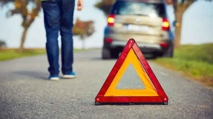 Triángulo de emergencia en carretera. Persona se aleja de coche averiado, lista para proteger, alertar y socorrer.