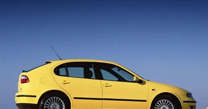 Żółty Seat Leon 2000, sportowy hatchback, zaparkowany na tle błękitnego nieba.
