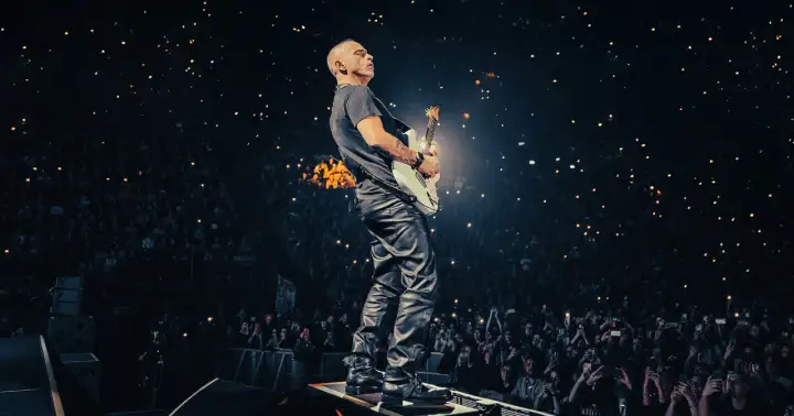 Eros Ramazzotti gra na gitarze podczas koncertu, a tłum w ciemnościach trzyma zapalone telefony.