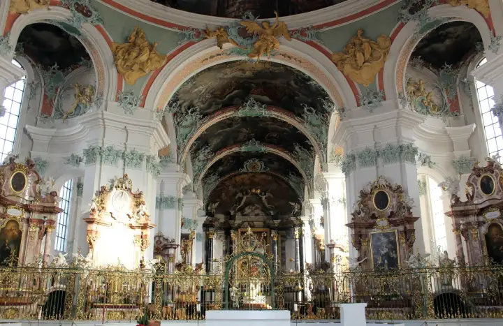 Wnętrze kościoła w stylu barokowym, z bogatymi zdobieniami, freskami na sklepieniach i złotymi elementami.