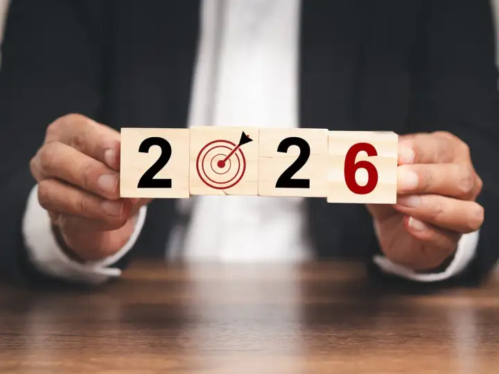 Ręce trzymają kostki z napisem "2026" i tarczą celowniczą. To symboliczne przedstawienie celów i planowania, jak środki trwałe co to, w kontekście przyszłości.