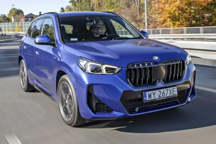 Niebieskie x1 bmw z kierowcą w okularach przeciwsłonecznych jedzie po drodze.
