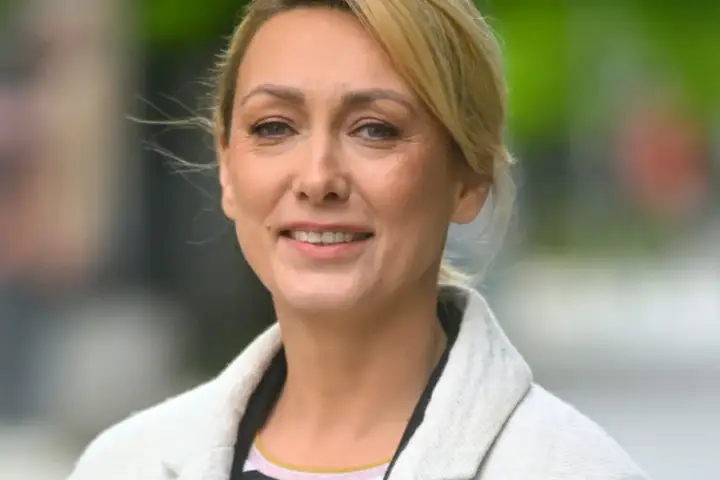 Portret uśmiechniętej blondynki w jasnym płaszczu.