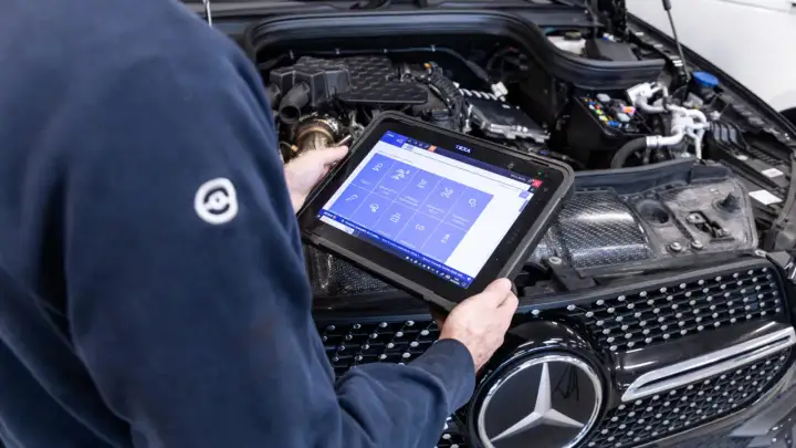 Tecnico esegue la revisione auto con tablet diagnostico, controllando i sistemi del motore.