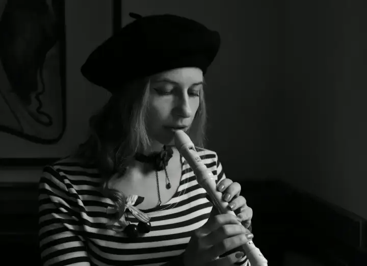 Kobieta w beretce gra na flecie. Pokazuje, jak się gra gamę na flecie, skupiona na melodii.