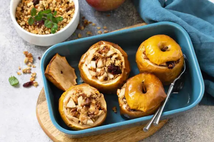 Mele cotte ripiene di frutta secca e granola, servite in una teglia blu.
