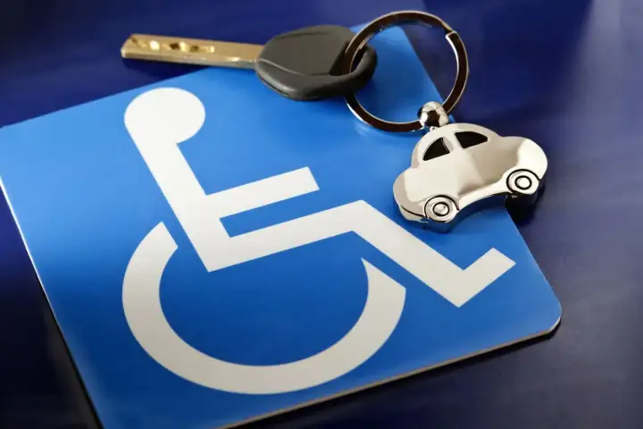 Chiave e portachiavi a forma di auto su un cartello blu con simbolo di disabilità, evocando l'invalidità civile 35 legge 104.