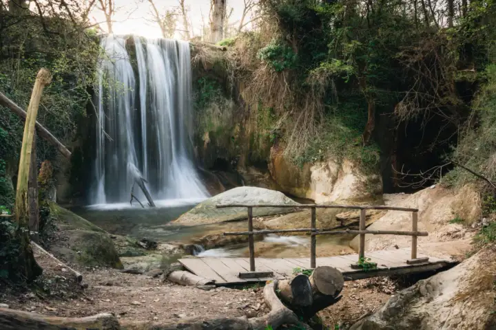 Cascata incantevole, le cascatelle di Sarnano creano un'atmosfera magica con la loro acqua impetuosa che scende tra rocce e vegetazione lussureggiante. Un piccolo ponte di legno invita all'esplorazione.