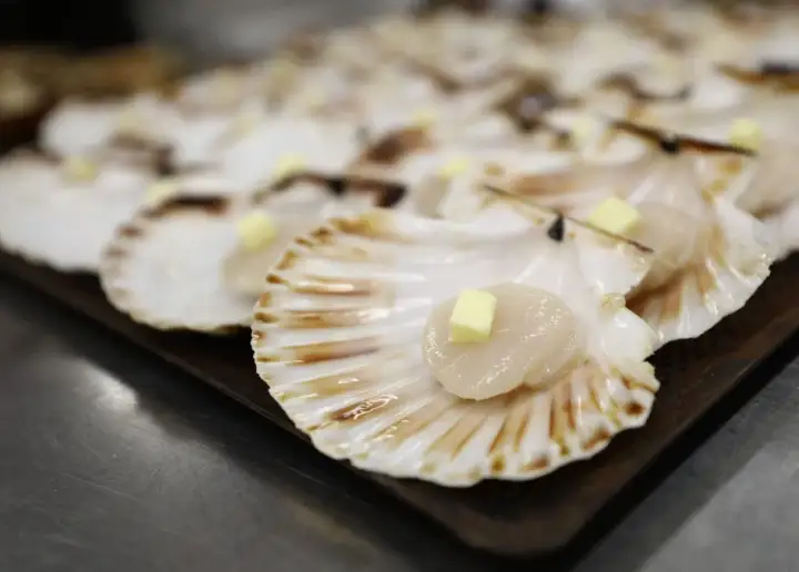 Coquilles Saint-Jacques prêtes à être cuisinées, chacune garnie d'un cube de beurre.