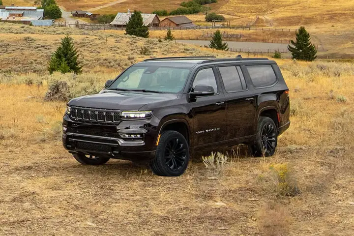 Ciemny Jeep Grand Wagoneer na tle wiejskiego krajobrazu z budynkami i drzewami.