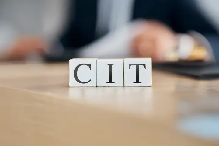 Trzy kostki z literami C, I, T układają się w napis CIT. W tle rozmyta postać pochylona nad dokumentami, sugerująca pracę nad podatkiem CIT.