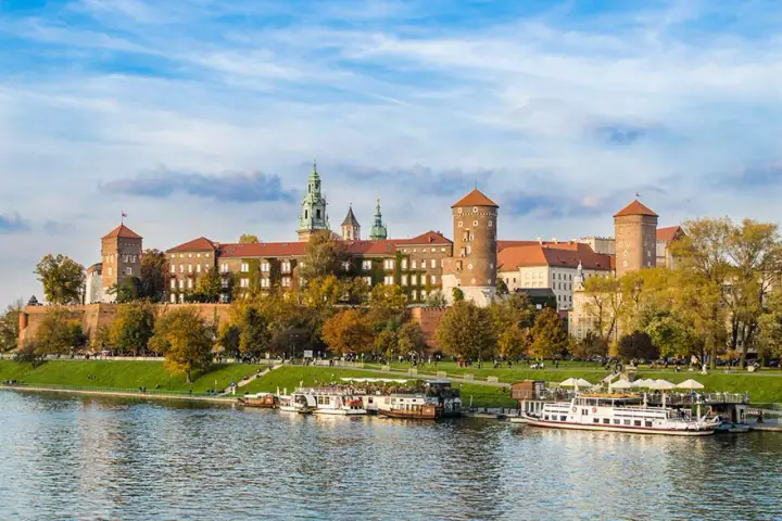 Zamek Królewski na Wawelu, majestatyczna budowla nad Wisłą, otoczona jesienną zielenią i błękitem nieba.