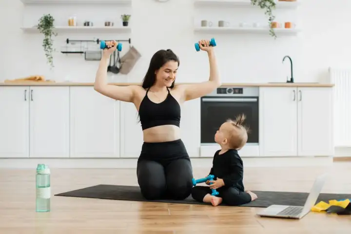 Mama i dziecko ćwiczą z hantlami w kuchni. To świetny przykład na 10 ćwiczeń z hantlami, które można wykonać w domu.