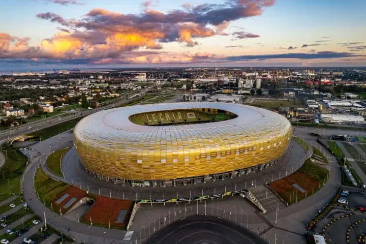 Stadion Energa w Gdańsku, znany jako Letnica Gdańsk, lśni złotem pod zachodzącym słońcem.