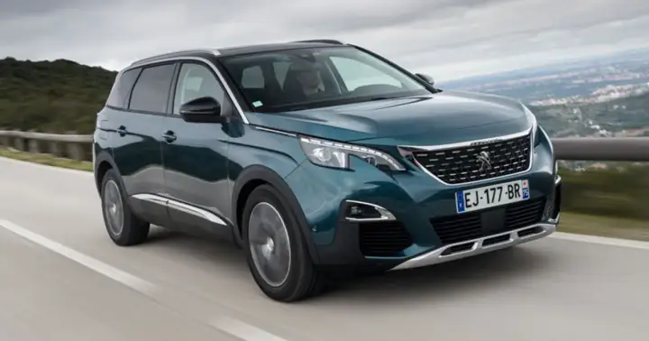 Peugeot 5008 wady i zalety: zielony SUV jedzie po krętej drodze z widokiem na góry.