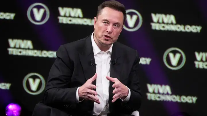 Elon Musk w garniturze, przemawiający na tle logo Viva Technology.
