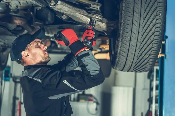 Mechanik w rękawicach dokręca sworznie w zawieszeniu samochodu.
