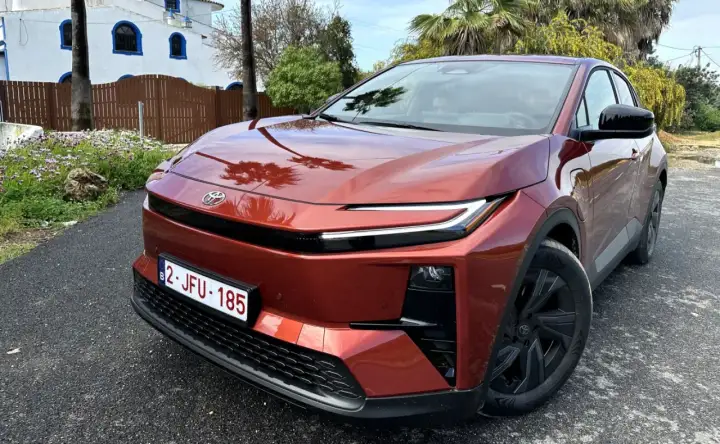 Nowa Toyota w kolorze miedzianym, zaparkowana przed białym budynkiem z niebieskimi oknami.