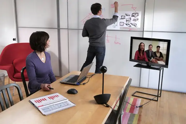 Spotkanie online, gdzie jakość SD a HD robi różnicę. Kobieta patrzy na ekran, mężczyzna pisze na tablicy.