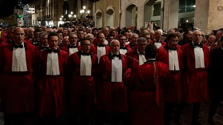 Uomini in toga rossa partecipano alla processione del Venerdì Santo a Sulmona, un momento di profonda spiritualità e tradizione.