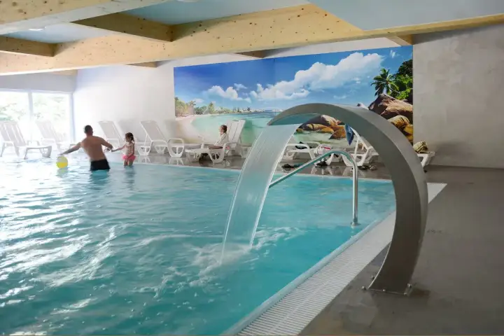 Rodzina bawi się w basenie z wodospadem w hotelu Pokrzywna. Relaks w gorzelnianym klimacie.