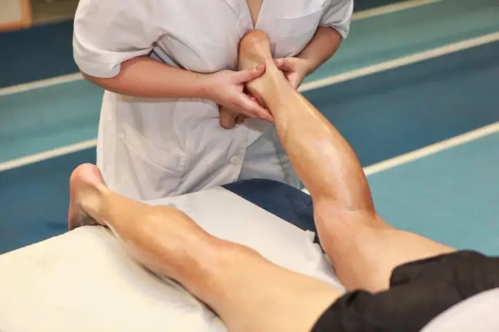 Fizjoterapeuta wykonuje masaż ścięgna Achillesa sportowca, łagodząc napięcie po treningu.