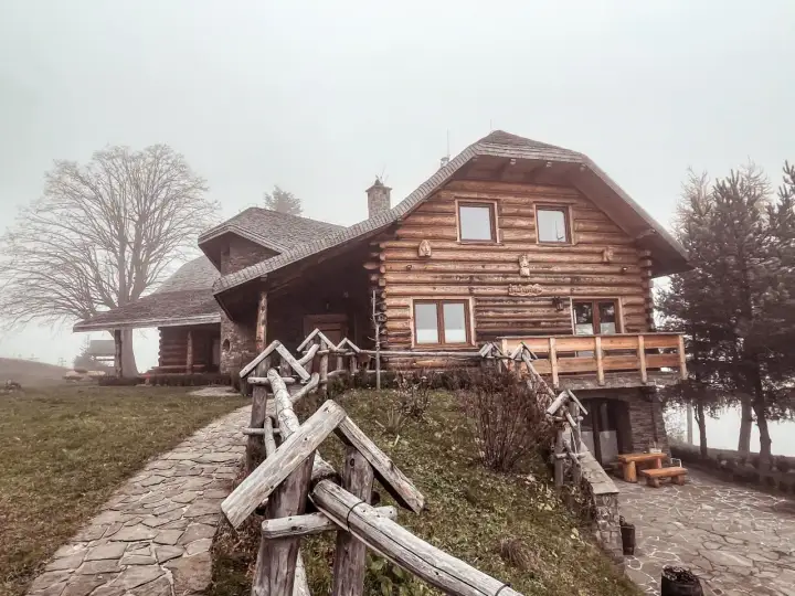 Drewniany dom z kamienną podstawą, kamienista ścieżka i płot. Mglisty dzień dodaje uroku temu miejscu, które oferuje liczne laskowa atrakcje.