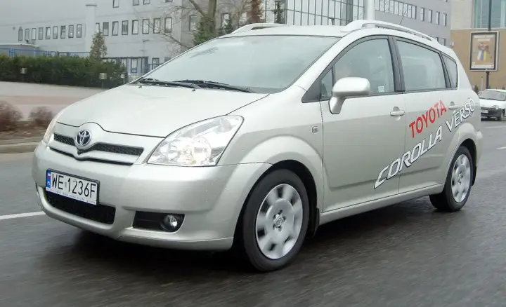 Srebrna Toyota Corolla Verso jedzie po mokrej drodze. Na drzwiach widnieje napis "Toyota Corolla Verso".