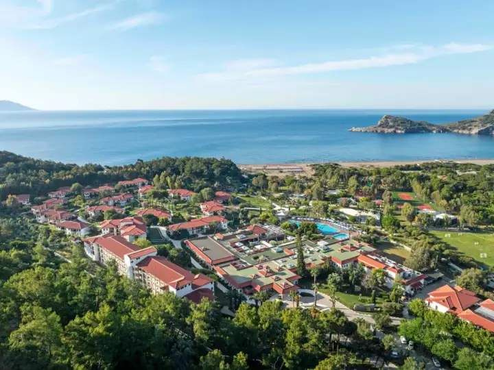 Luftaufnahme des TUI Blue Sarigerme Park mit Blick auf das Meer, Pools und Tennisplätze, eingebettet in üppige grüne Bäume.